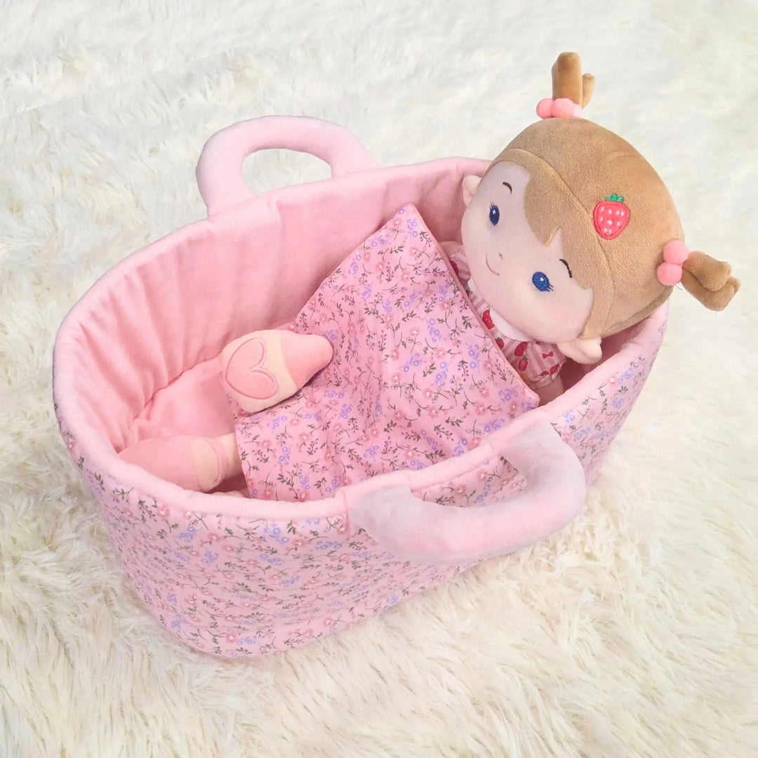 Strawberry Girl plush doll lying in 13-inch Caregiver Playset bassinet with matching blanket for pretend doll care