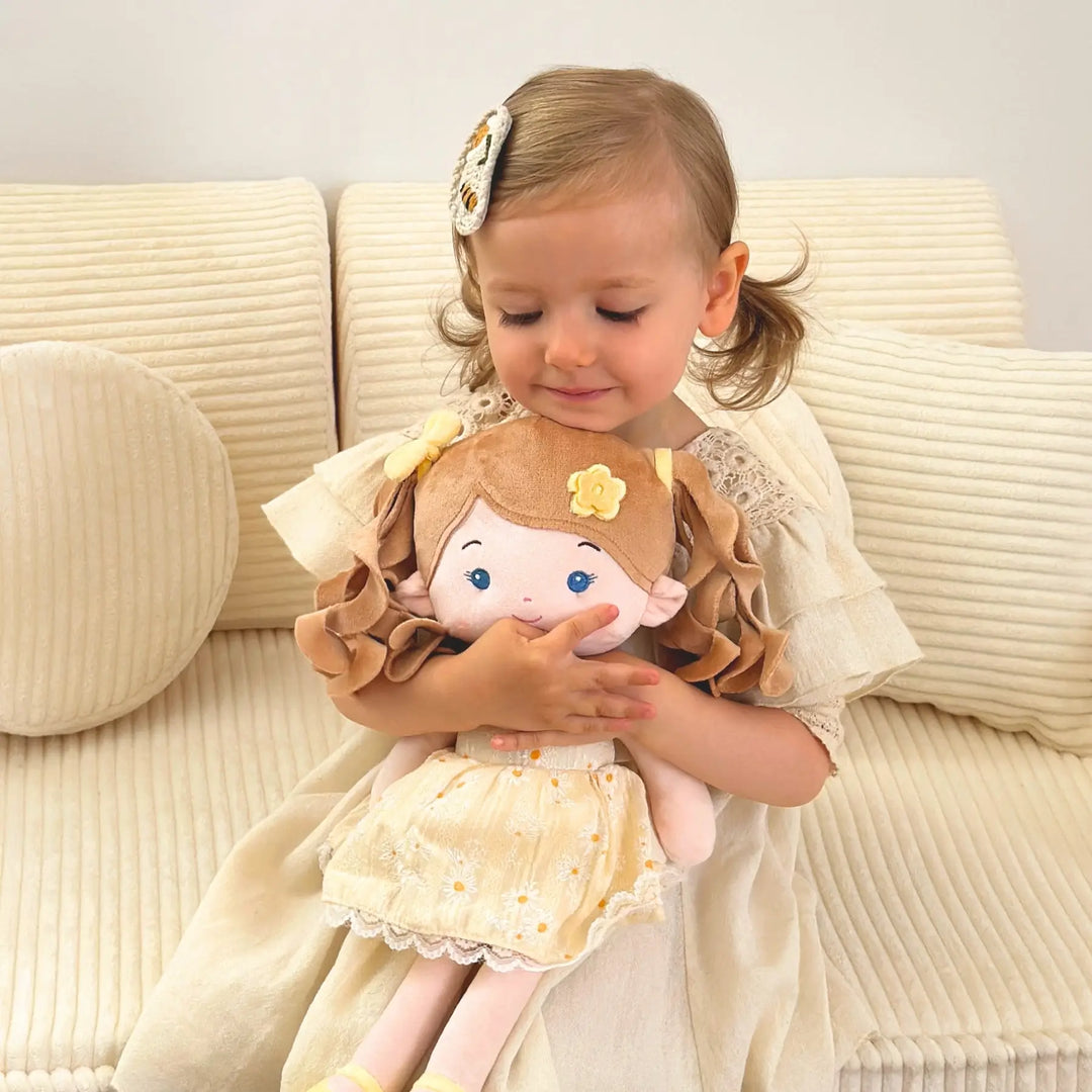 Baby girl hugging Daisy Girl plush doll during playtime on a sofa