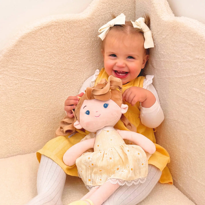 Baby girl cuddling Daisy Girl plush doll while smiling in a chair